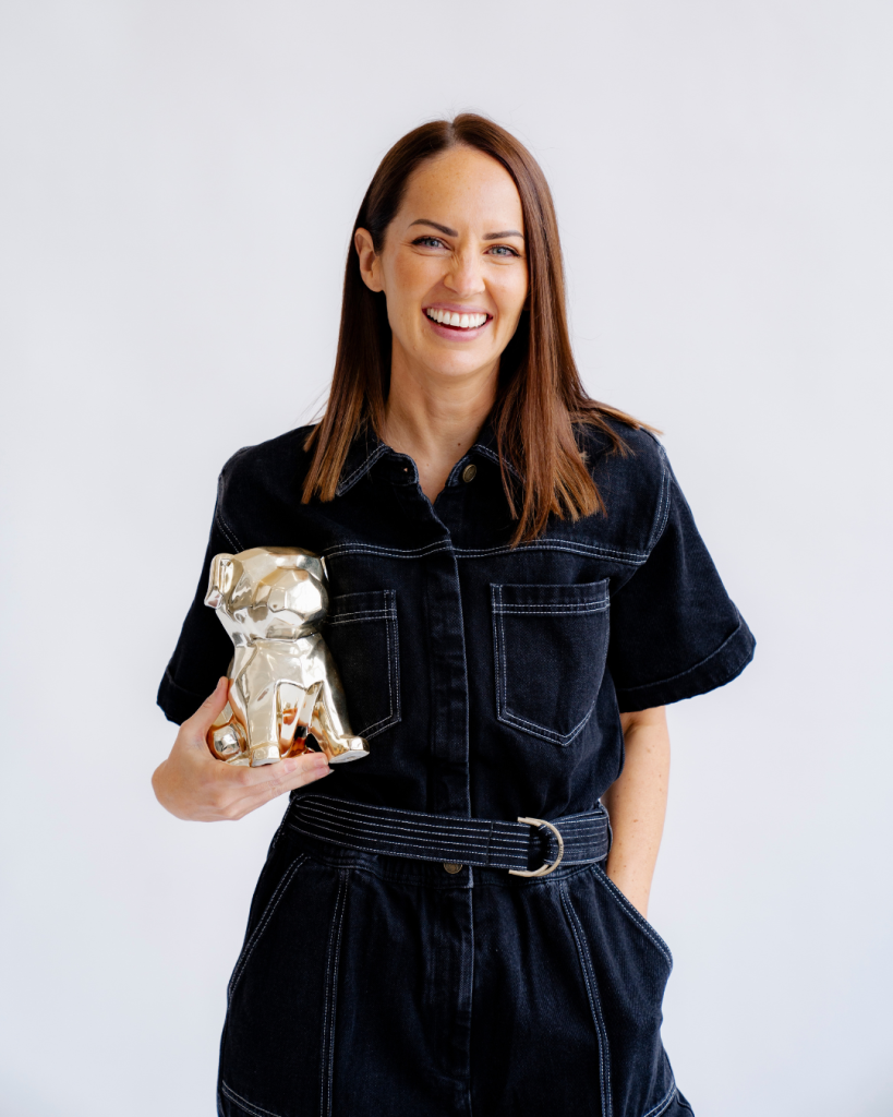Carinda Gosling smiling and holding a gold dog statue - a stand-in for her dog Evie